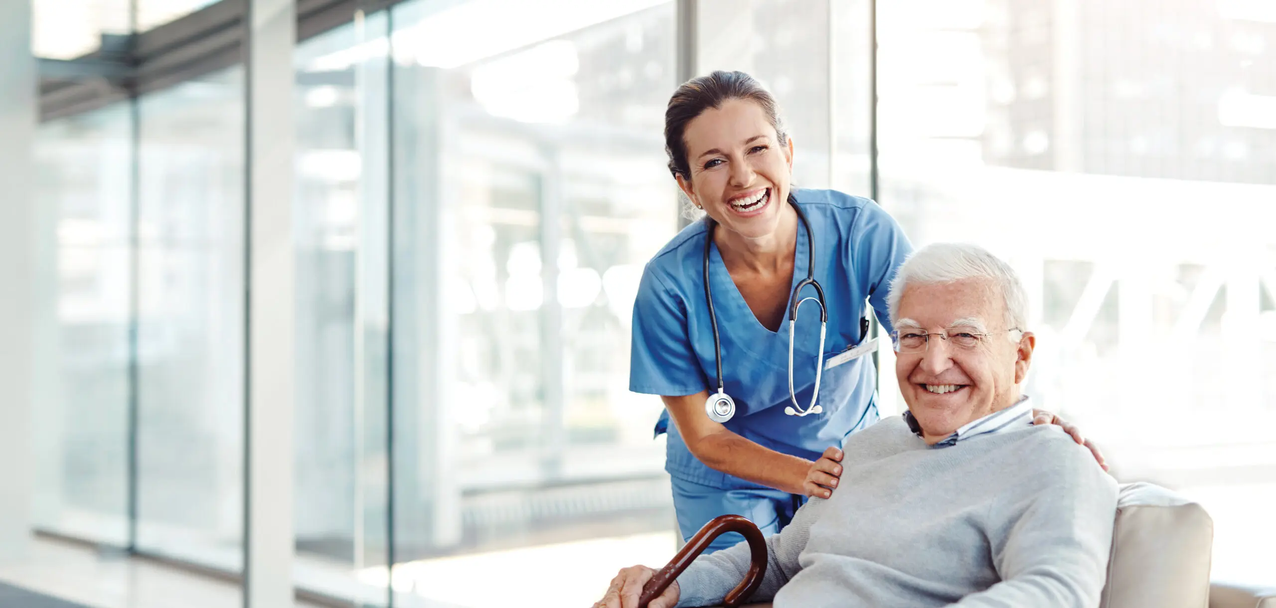 A healthcare worker smiles with an older man, who is seated.