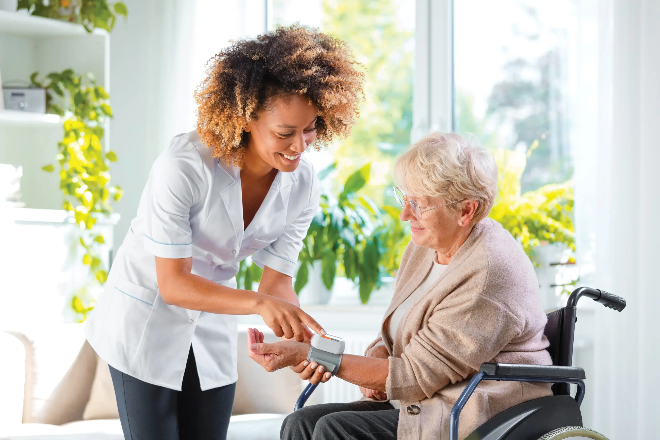 A home nurse checks the blood pressure of a woman in a wheelchair. They both look happy and content.