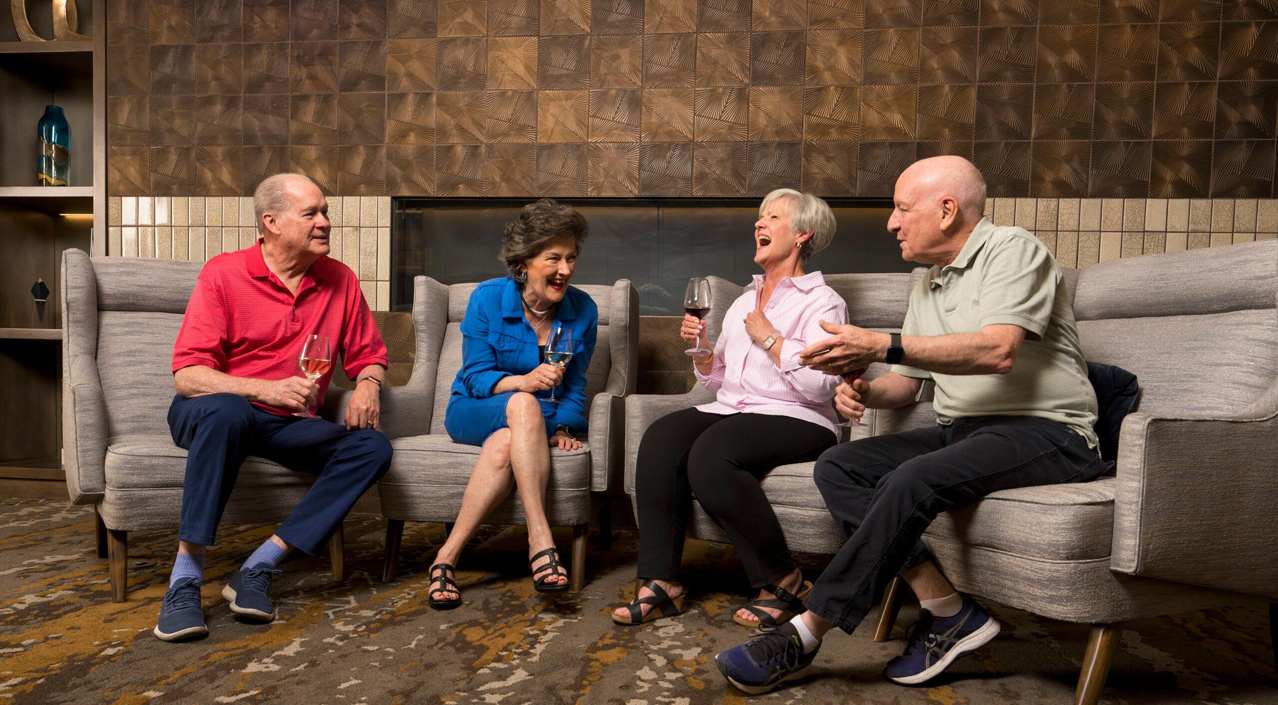 A group of four older adults talk and laugh over glasses of wine.